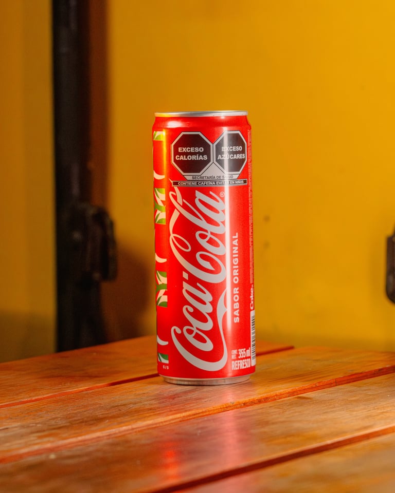 A red Coca-Cola can on a wooden surface against a yellow background