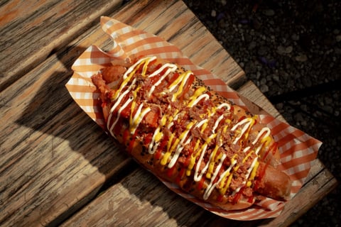Grilled hot dog topped with mustard and ketchup drizzle, served on orange checkered paper on a wooden surface