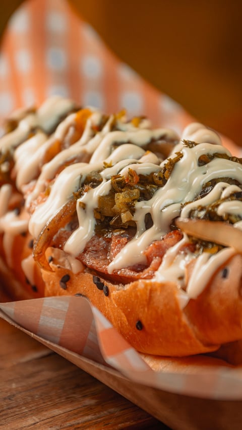 Gourmet hot dogs topped with caramelized onions and creamy white sauce on a wooden plate with orange checkered napkin