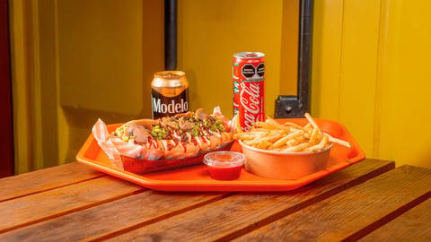 A meal tray with nachos, hot dog, fries, beer, and soda on a wooden table against a yellow wall