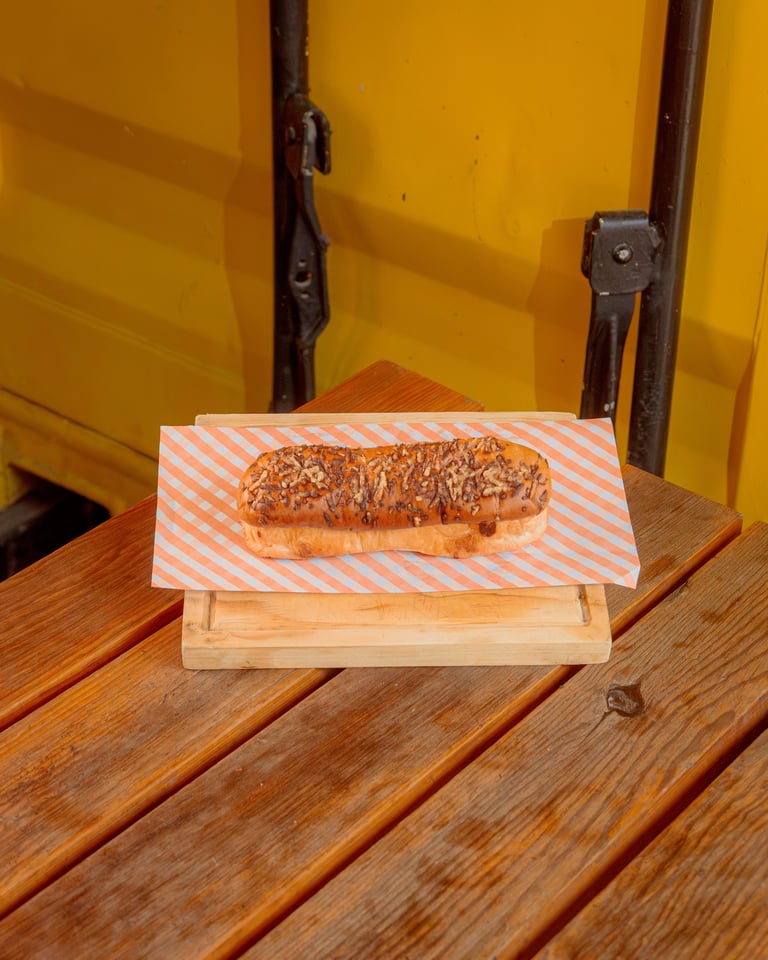 A seeded bagel sandwich on striped paper sits on a wooden board against a bright yellow wall