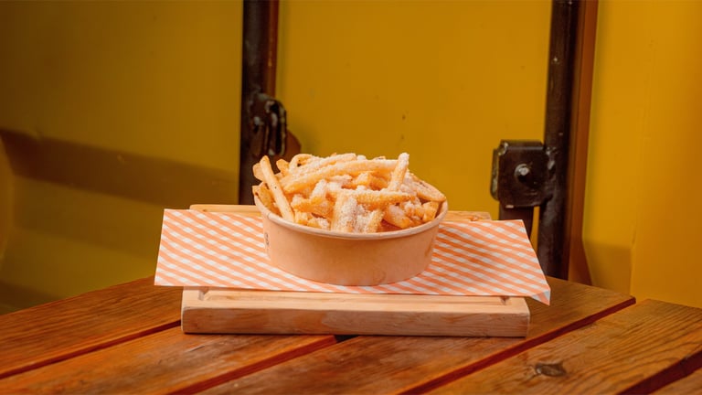 Basket of French fries on a pink and white striped paper liner placed on a wooden table against a yellow wall
