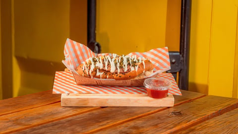 Eclair with white drizzle on pink striped paper, wooden serving board, yellow wall background with beverage