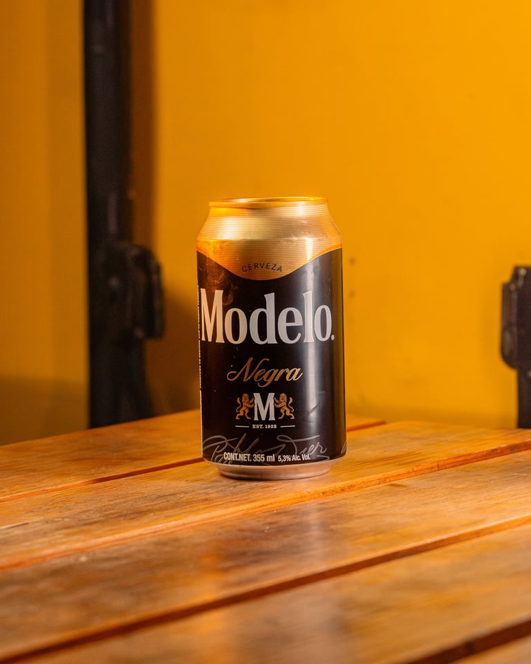 A can of Modelo Negra beer sitting on a wooden table against a bright yellow background