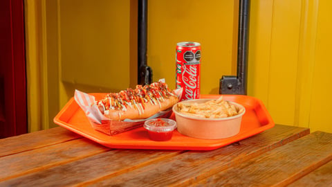 Fast food meal on orange tray with hot dog, drink, fries, and sauce on wooden table against yellow wall