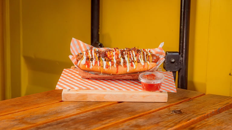 Lobster tail drizzled with sauce on striped paper, served on wooden table against yellow wall with garnish sauce