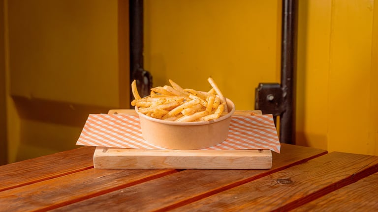 Golden french fries in a cardboard container on a wooden table against a yellow wall