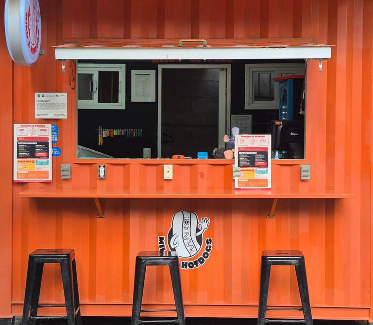 Orange food truck exterior with service window, three metal stools, and vendor signage