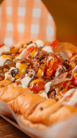 Gourmet hot dogs topped with bacon, peppers, and white sauce on a checkered napkin