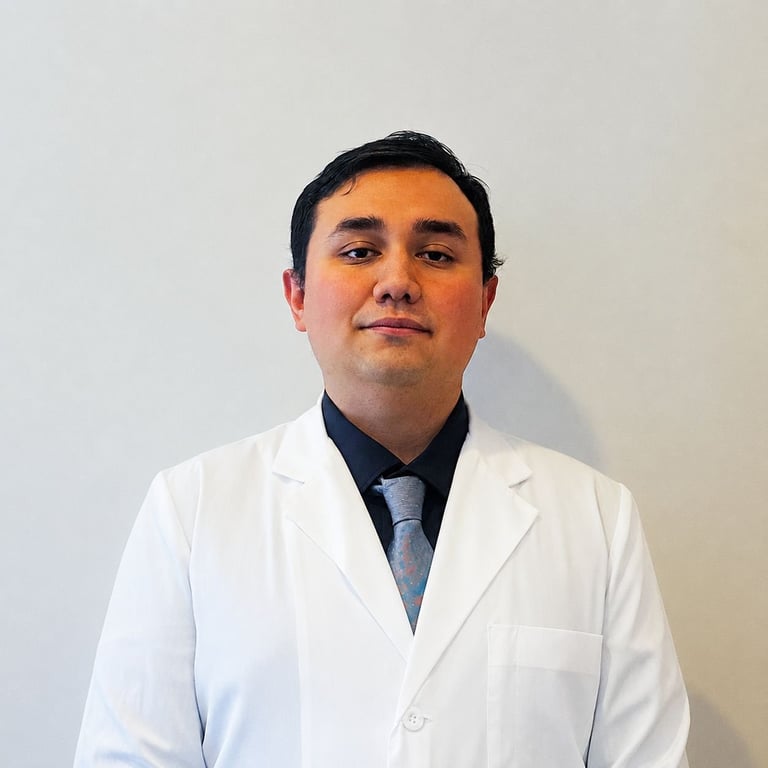 Male healthcare professional wearing white lab coat and dark shirt with tie, standing against neutral background